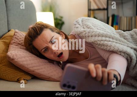 Woman experiencing shock while looking at phone in bed Stock Photo