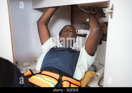 Plumber fixing pipes under the sink in the kitchen Stock Photo