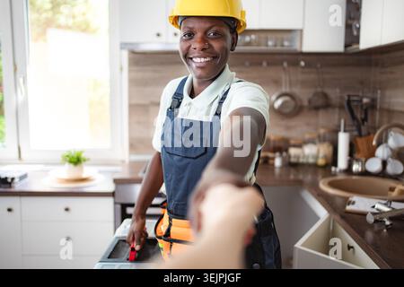 Smiling african american female plumber shaking hands after finishing work in kitchen Stock Photo
