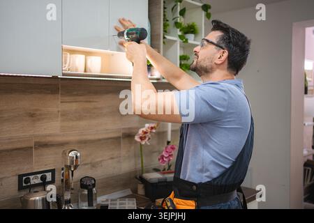 Handyman installing kitchen cabinets using a cordless screwdriver Stock Photo