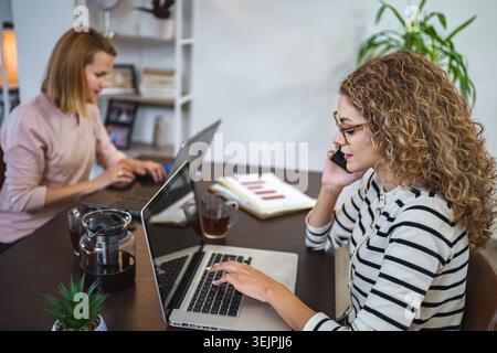 Two female colleagues at a desk working on laptop Stock Photo