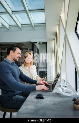 Professionals collaborating on laptop and digital tablet in modern office Stock Photo