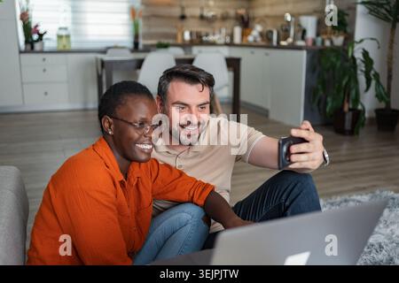 Happy couple taking a selfie at home using a smartphone Stock Photo