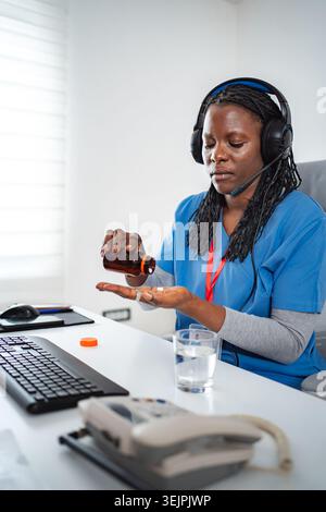 Healthcare worker taking pills at telehealth office desk Stock Photo