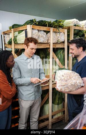 Warehouse workers managing fresh vegetables with digital tablet Stock Photo