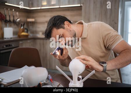 Technician repairing cctv camera using smartphone flashlight in kitchen Stock Photo