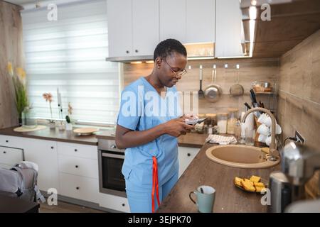 Nurse using smartphone in kitchen during break time Stock Photo