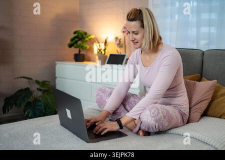 Woman working on laptop in bed wearing pajamas Stock Photo