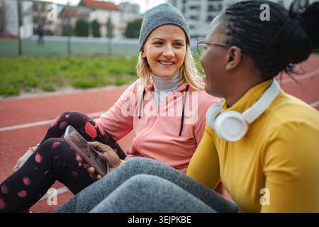 Diverse women friends resting and talking on running track Stock Photo