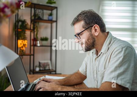 Focused man working on his laptop in a cozy workspace Stock Photo