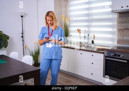 Female Doctor Using Smartphone at Home in her Kitchen Stock Photo