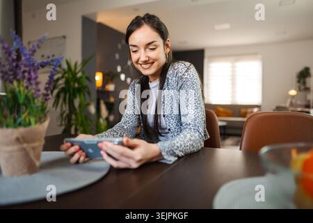 Happy relaxed young woman using mobile phone in living room Stock Photo