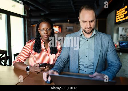 Colleagues working together at a cafe, using a laptop and smartphone Stock Photo
