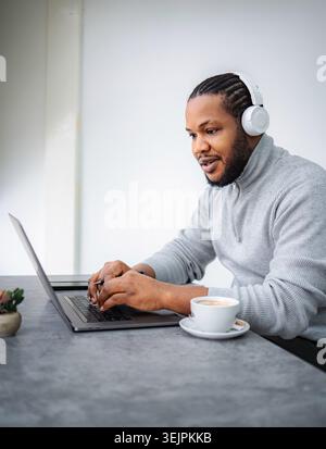 Black man wearing headphones working on laptop at cafe Stock Photo
