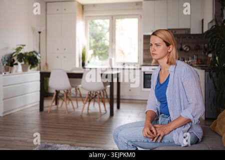 Young woman sitting on sofa feeling lonely at home Stock Photo