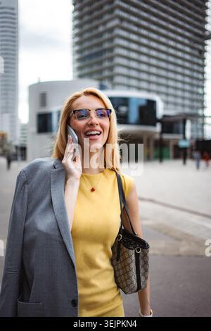 Businesswoman talking on phone walking in city smiling Stock Photo