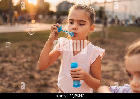 Girl blowing soap bubbles in a park at sunset Stock Photo