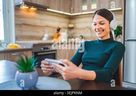 Young Woman Relaxing at Home, Watching Videos on Smartphone and Listening to Music with Headphones Stock Photo
