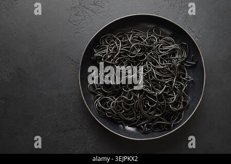Black pasta spaghetti squid Ink in black bowl on black. Top view. Space for text. Stock Photo