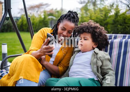 Mother and son relaxing outdoors using smartphone together Stock Photo
