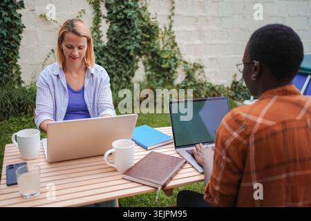 Two colleagues working outdoor with laptops on a wooden table Stock Photo