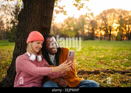 Diverse friends taking a selfie using smartphone in autumn park Stock Photo