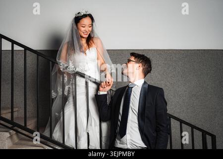 Interracial couple holding hands on stairs after wedding Stock Photo