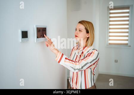 Woman interacting with smart home control panel displaying security camera Stock Photo