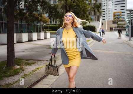 Happy young woman running laughing on city street Stock Photo