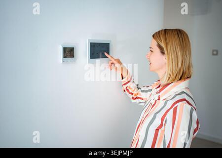 Woman adjusting smart home thermostat touchscreen for comfort Stock Photo