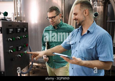 Brewery workers operating control panel in production facility Stock Photo