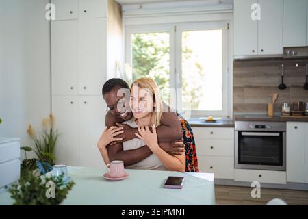 Two cheerful female friends are hugging in the kitchen Stock Photo