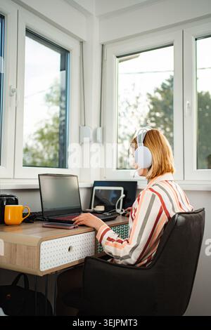 Woman working from home connecting with laptop and headphones Stock Photo