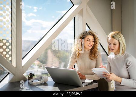 Two women collaborating on laptop and paperwork in modern office Stock Photo