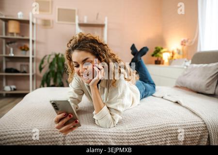 Young woman relaxing in bedroom using smartphone Stock Photo