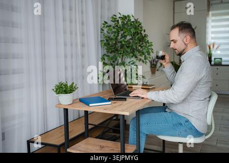 Mid-adult man drinking coffee while working on laptop at home Stock Photo