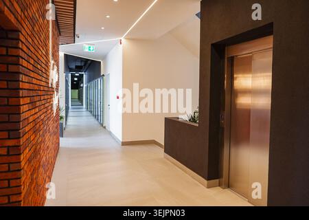 A long hallway is shown in the image, featuring a prominent metal door on one side and a planter on the other. The hallway stretches into the distance Stock Photo