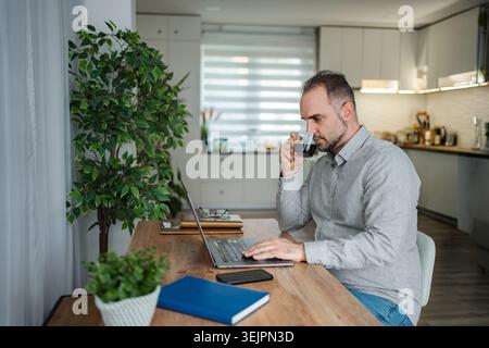 Man drinking coffee working on laptop from home office Stock Photo