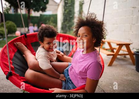 Happy siblings smiling sitting together on swing Stock Photo