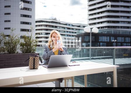 Young businesswoman using smartphone and laptop for remote work Stock Photo