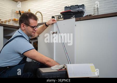 Man installing new kitchen cabinets using a measuring tape Stock Photo