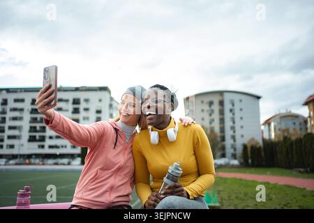 Two happy multiracial women friends taking a selfie after sport on a running track Stock Photo