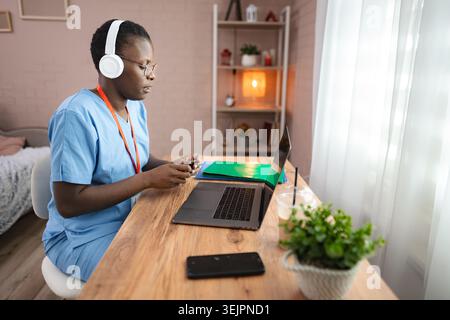 Focused female doctor working from home using laptop and smartphone Stock Photo