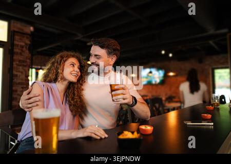 Couple enjoying drinks and snacks at a bar, looking at each other lovingly Stock Photo
