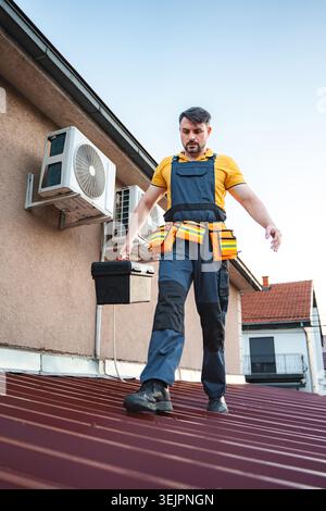Technician walking on roof while carrying toolbox and inspecting air conditioning units Stock Photo