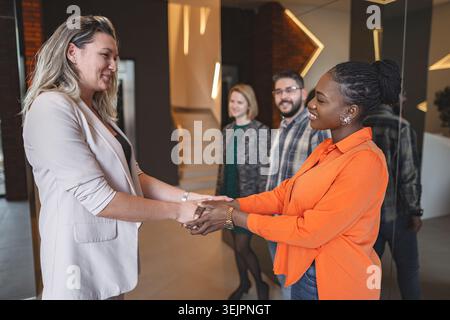 Two Women Shaking Hands in Front of a Group of People Stock Photo