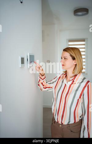 Woman adjusting smart home automation system on wall control panel Stock Photo