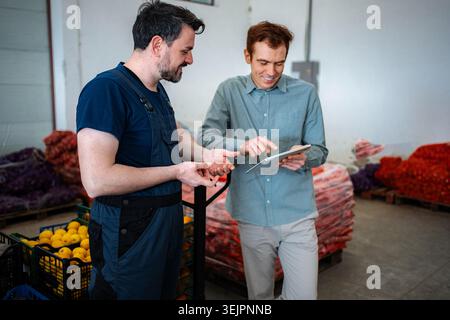 Two men working in a warehouse, using a digital tablet for inventory management Stock Photo