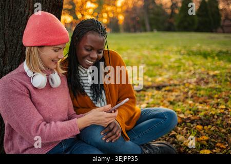 Diverse friends laughing sharing smartphone content outdoors Stock Photo