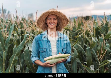 Farmer holding corn cobs and smiling in a cornfield Stock Photo